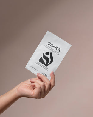 Hand holding a SIMKA product package against a beige background