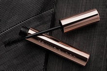 Bronze mascara tube with black wand on a textured black background