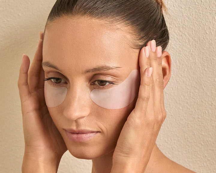 Woman applying eye patches with a neutral background